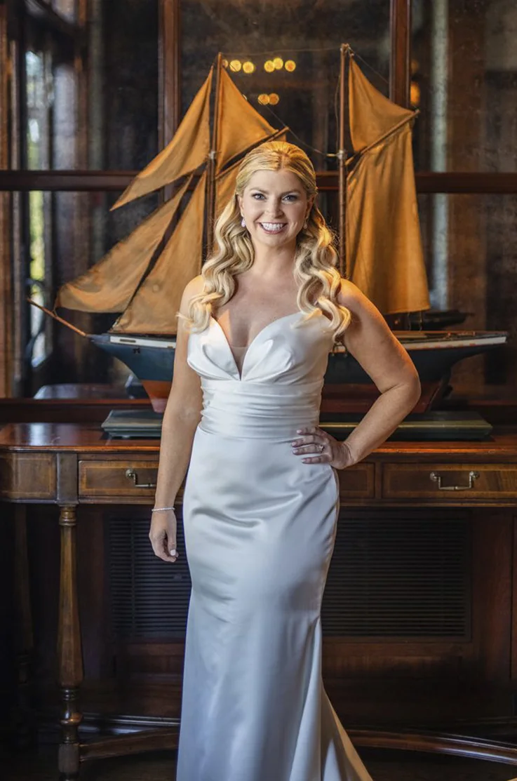 Bride poses in a satin fit and flare wedding dress with a plunging neck and ruched bodice in an elegant interior.