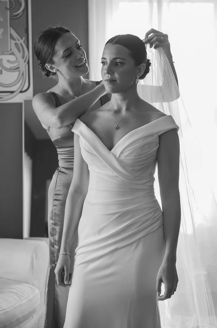 Bride gets ready in bridal suite in an off-the-shoulder crepe fitted gown with draping and a veil in black and white.