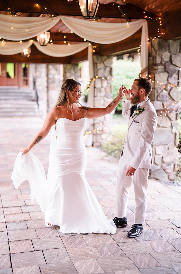 Bride in a mermaid ruched crepe gown with a veil, dances with her groom on outdoor pavilion.