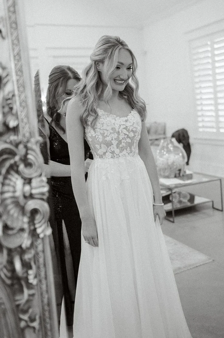 Bride gets ready in a lace bodice wedding dress with an organza skirt, looking in a mirror in a bridal suite