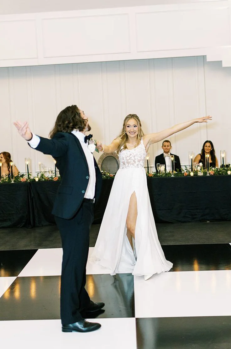 Bride in a lace and soft organza gown with a scoop neckline and thin straps, dances with groom on a checkered dance floor.
