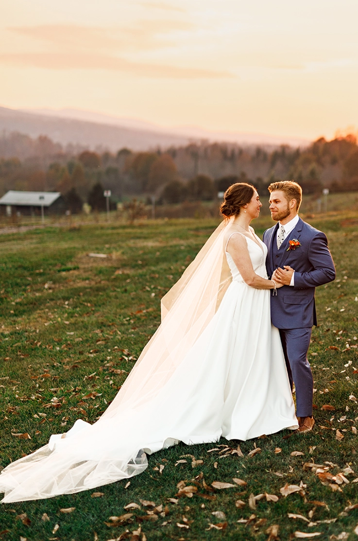 Bride in a sleeveless satin faille wedding dress with a flowing A-line skirt and veil, embracing groom on a hill.