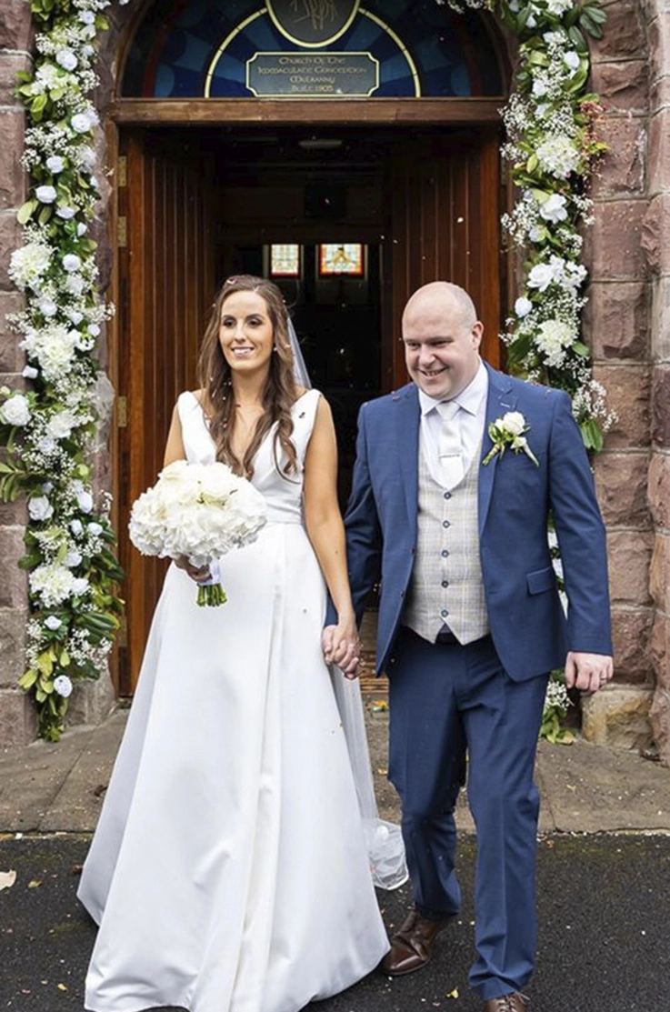 Bride in a draped satin faille bodice gown with a plunging neck and veil, walks out of the venue holding hands with groom.