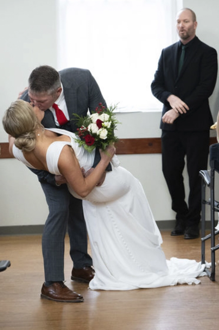  Groom dips his bride in a fitted crepe gown with a draped bodice and buttoned back, as they kiss.