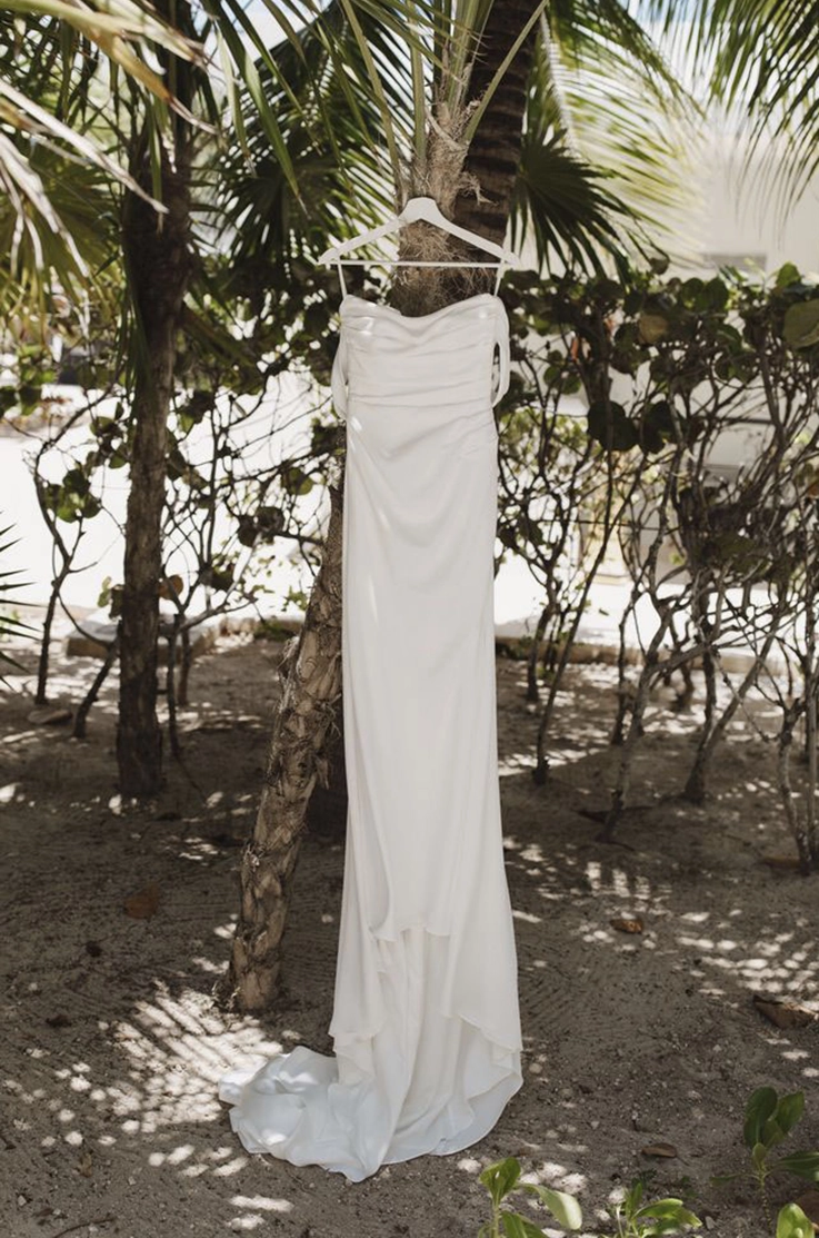  strapless draped crepe wedding dress with off-shoulder sleeves and a scoop neckline, hangs on palm trees on a beach.