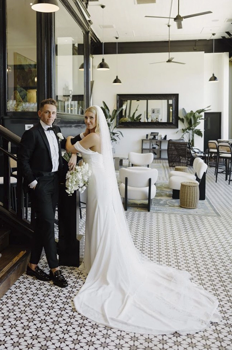 Bride in a crepe fit and flare gown with sleeves and a veil, poses with groom at the bottom of stairs