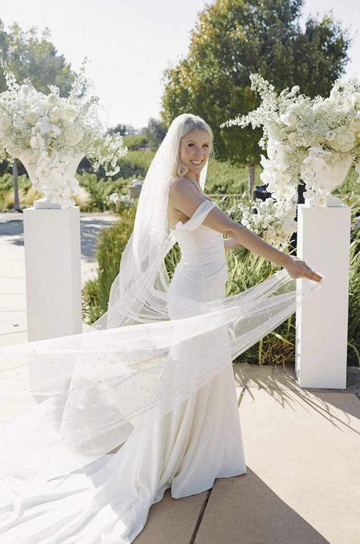  Bride twirls in an off-shoulder crepe fitted gown with a long flowing veil at an outdoor garden.