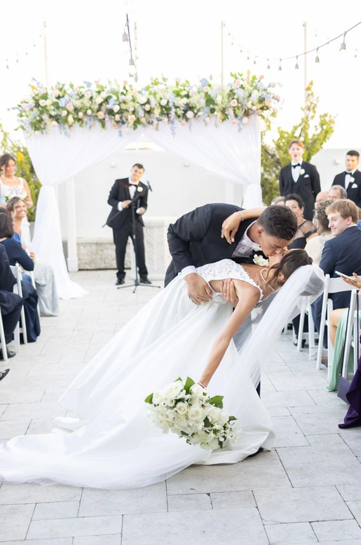 Groom dips his bride in a lace bodice wedding dress with an organza skirt and veil, and they kiss in the aisle.