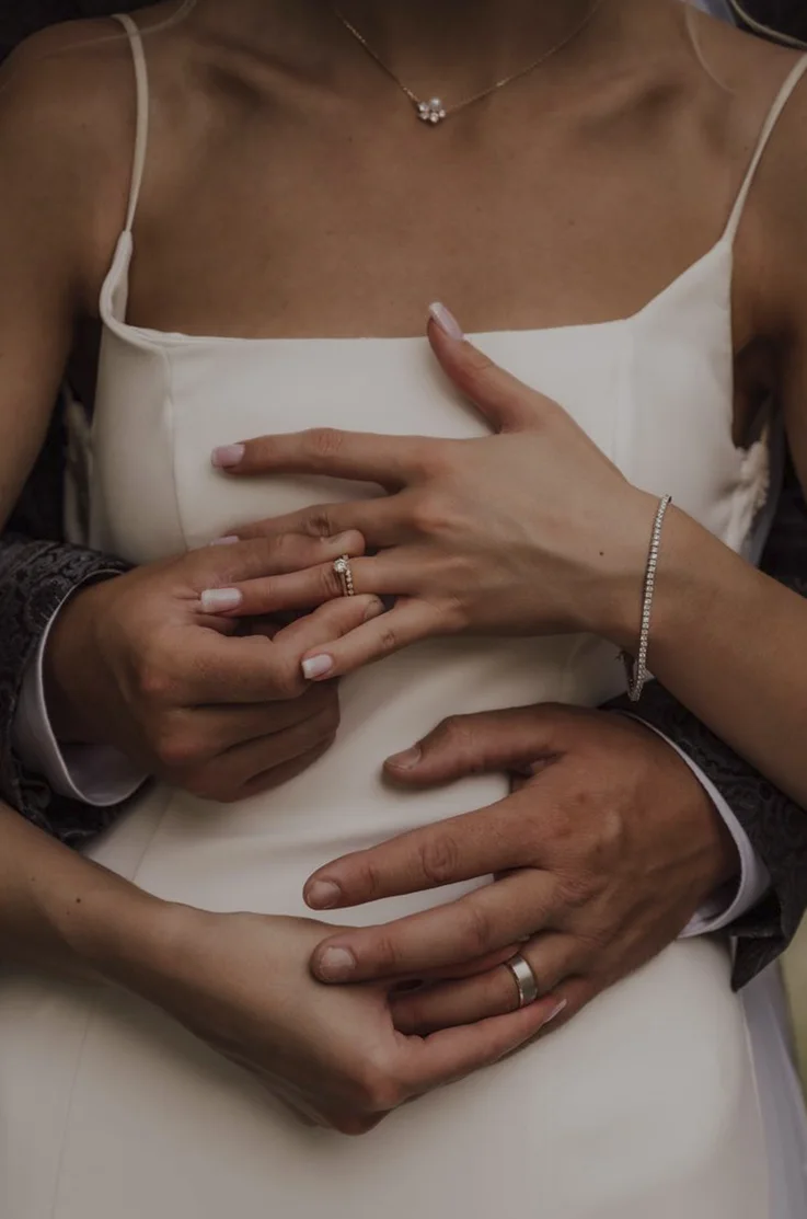 Close up of groom embracing bride in a scoop neck crepe gown with thin straps, as they put on their rings.