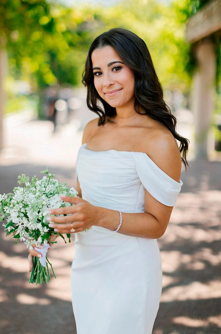 Close-up of bride in a draped satin bodice gown with fit and flare skirt and off-shoulder sleeves, smiling in a sunny park.