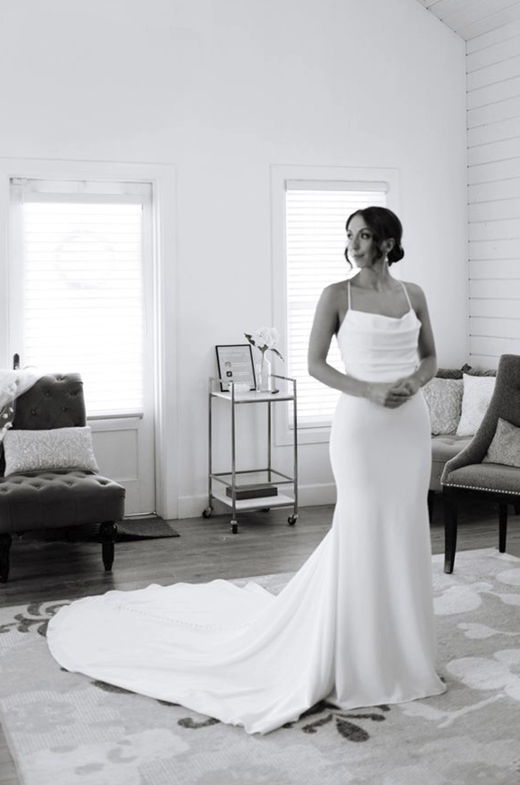 Bride poses indoors in a crepe pleated bodice gown with fit and flare skirt and a scoop neckline, shown in black and white. 