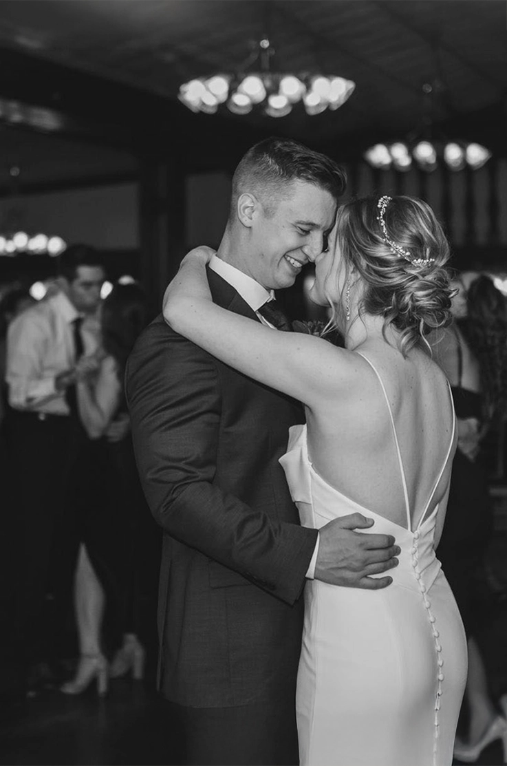Groom holds bride in an embrace dancing, in a low back fitted crepe gown with buttons and thin straps in black and white.