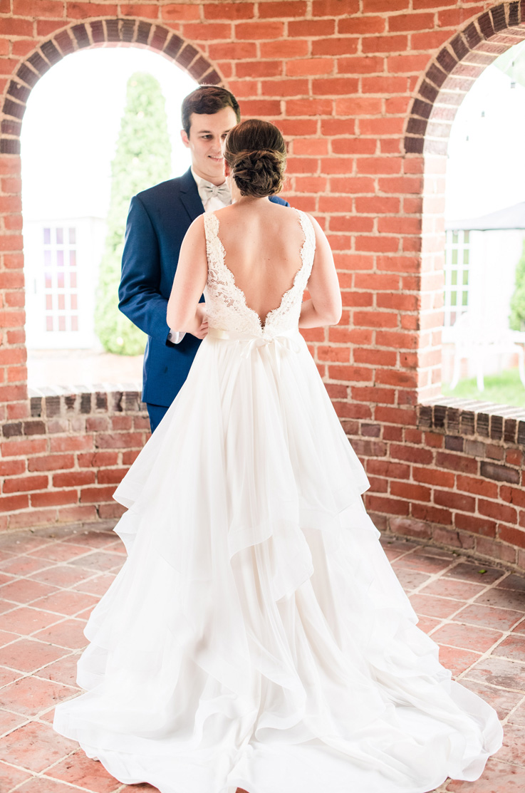 A bride in a tulle skirt wedding dress faces a groom in a suit, standing in a circular brick room with arched windows.
