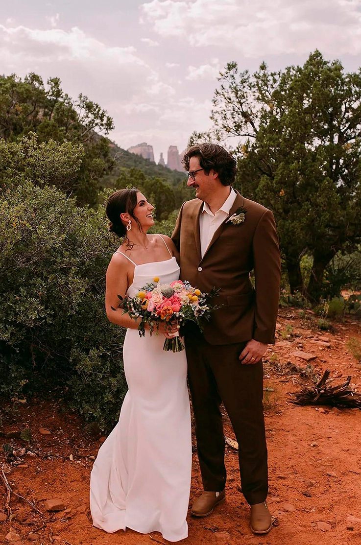 Bride in a spaghetti strap fitted gown with a scoop neckline, faces her groom in front of desert plants in a canyon.