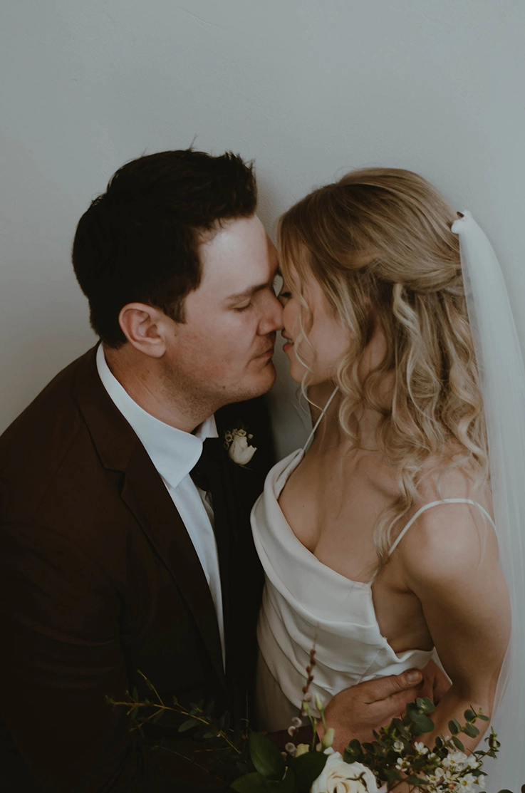Close-up of groom holding bride in an embrace in a scoop neck crepe gown with thin straps, a veil and pleating.