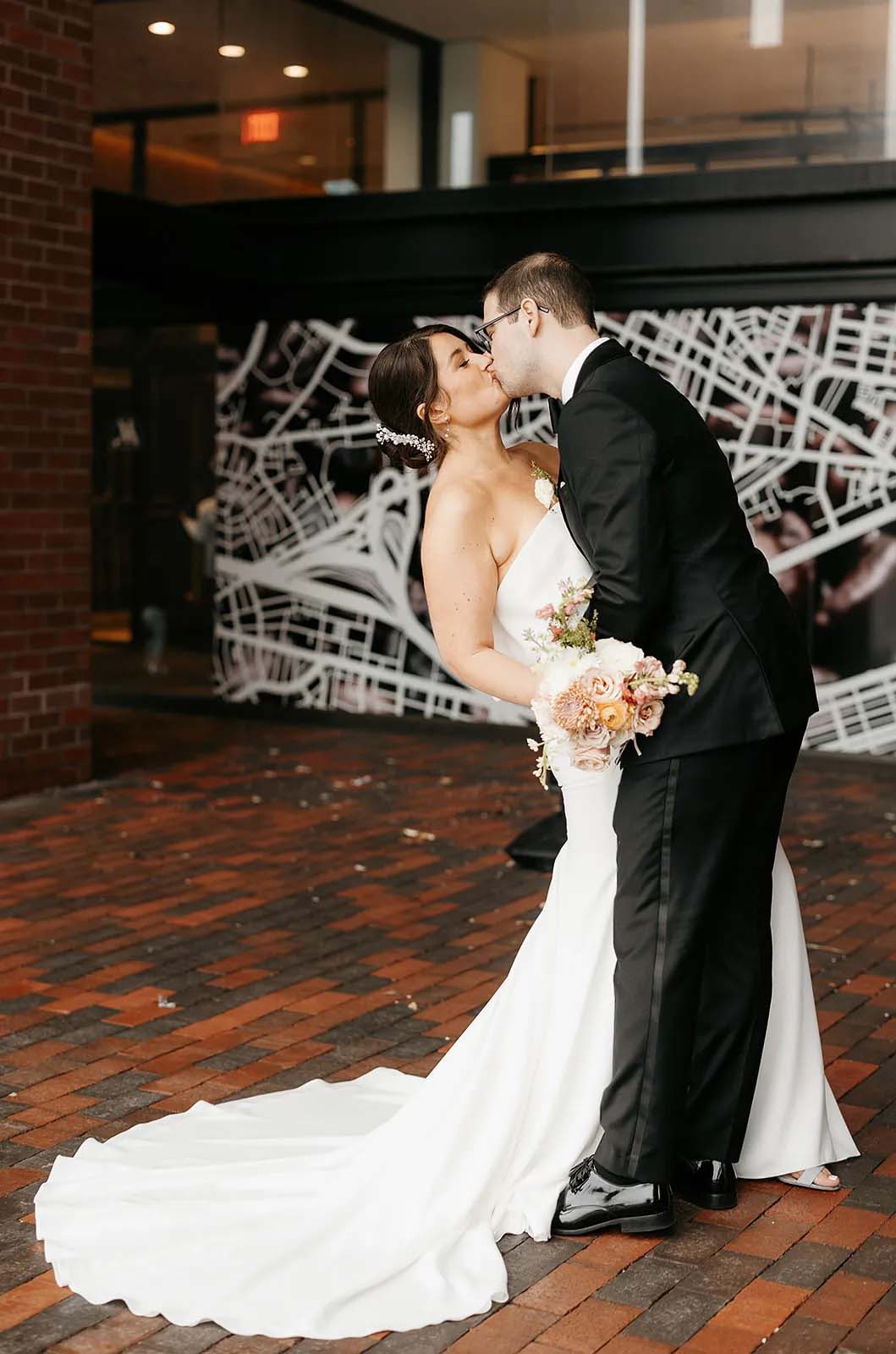 Groom dips his bride in a crepe fit and flare wedding dress with a portrait collar and they kiss at a modern venue.