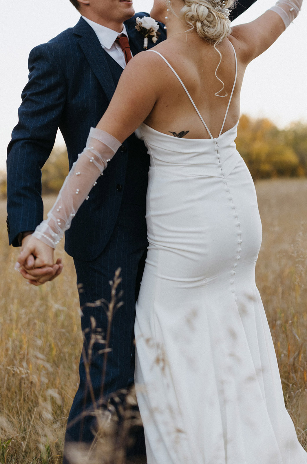 Close-up of bride in a fitted crepe gown with pleating, a buttoned back and beaded sheer gloves, dance in a wheat field.