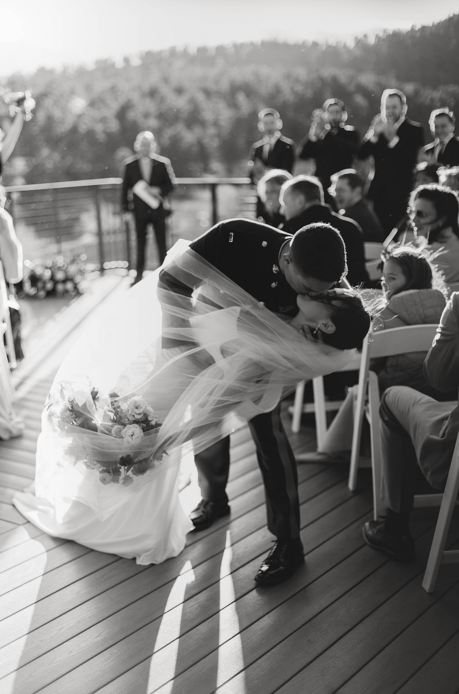 Groom dips his bride in a crepe fitted gown with a scoop neck and holds a bouquet under her veil in the aisle.