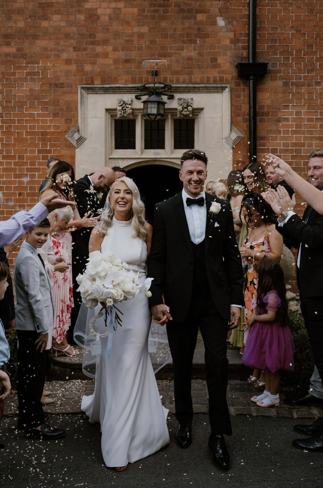Bride in a collared halter neck gown with fit and flare skirt, walks hand in hand with groom holding a bouquet as they exit. 