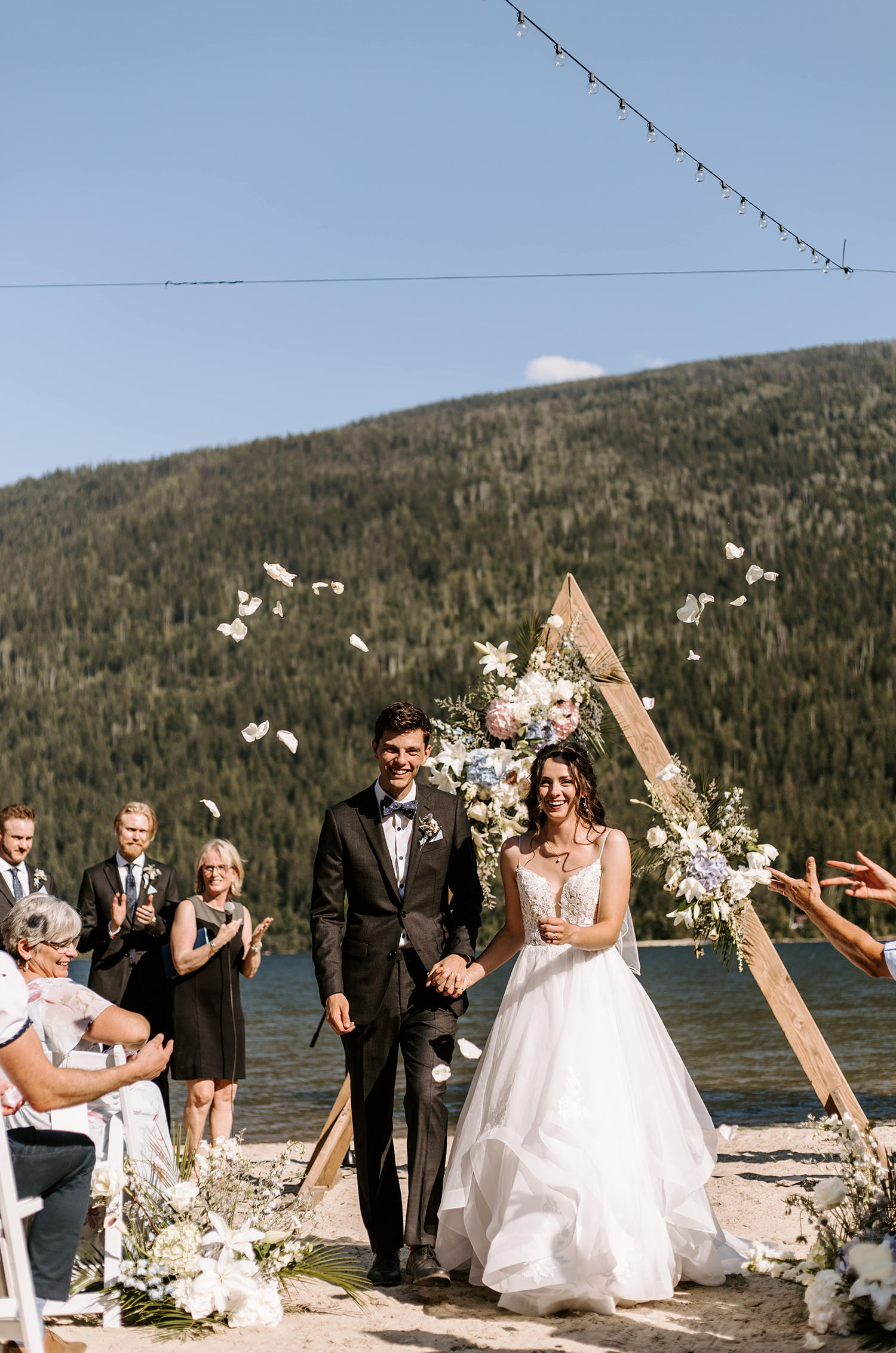 Bride in a lace bodice ballgown with a layered organza skirt, walks down the aisle with groom at a beach ceremony. 