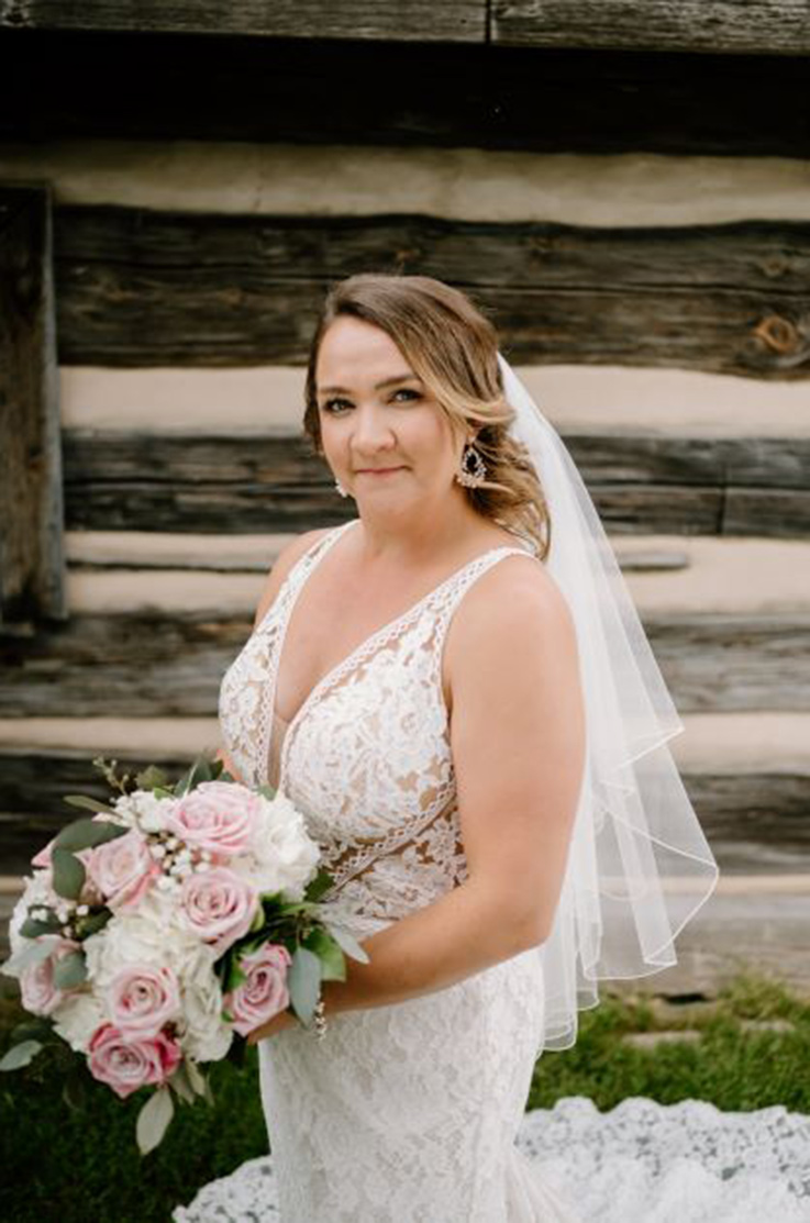 lose-up of bride posing in a fit and flare lace gown with a plunging neck, tulle lining and a veil, holding a bouquet.