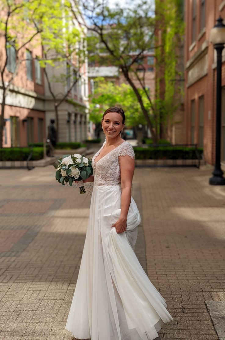 Bride in a deep-V back cap sleeved gown with tulle and an embroidered sequin bodice, twirls in a brick courtyard.