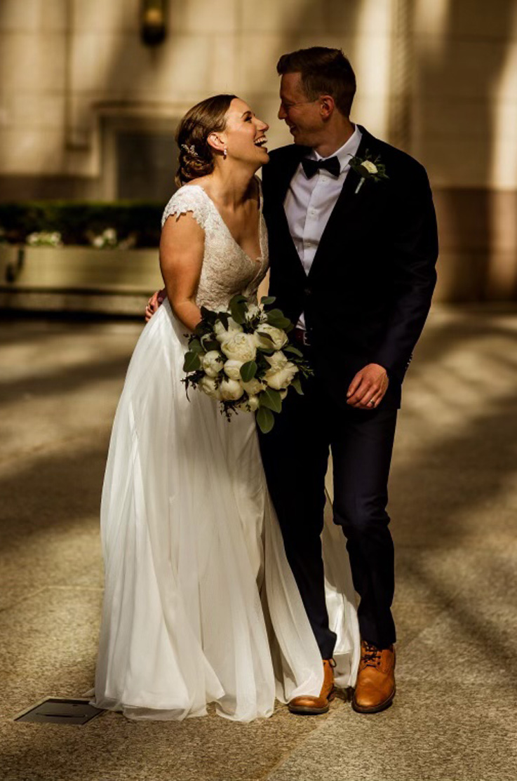 Bride in a plunging neck gown with a sheer sequin applique bodice and a flowing tulle skirt, laughs with her groom outdoors.