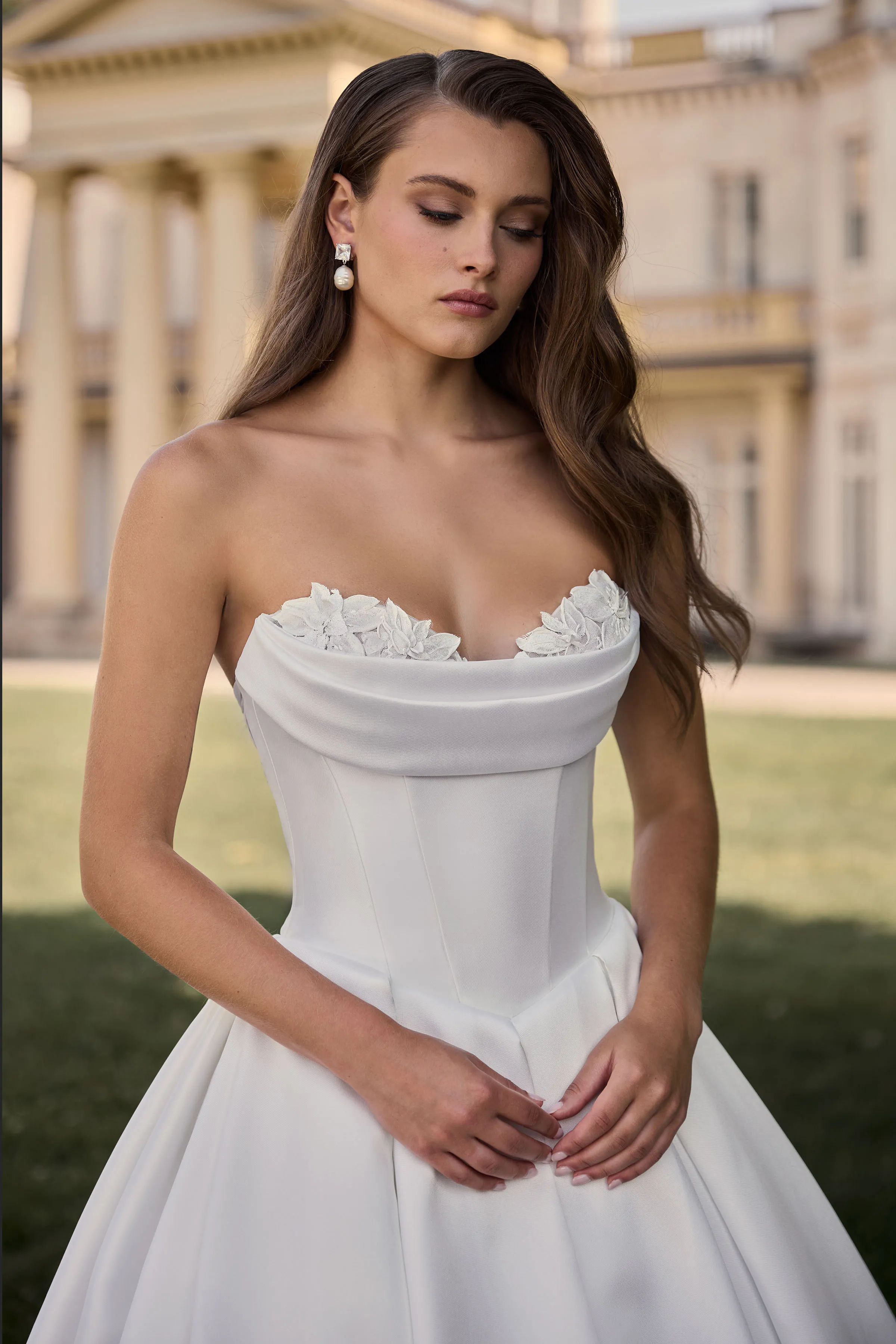 Close up view of a strapless Satin ball gown wedding dress with a lace sweetheart neckline and neckline drape with Basque waistline and pleated skirt, outside in the grass in front of a large manor.