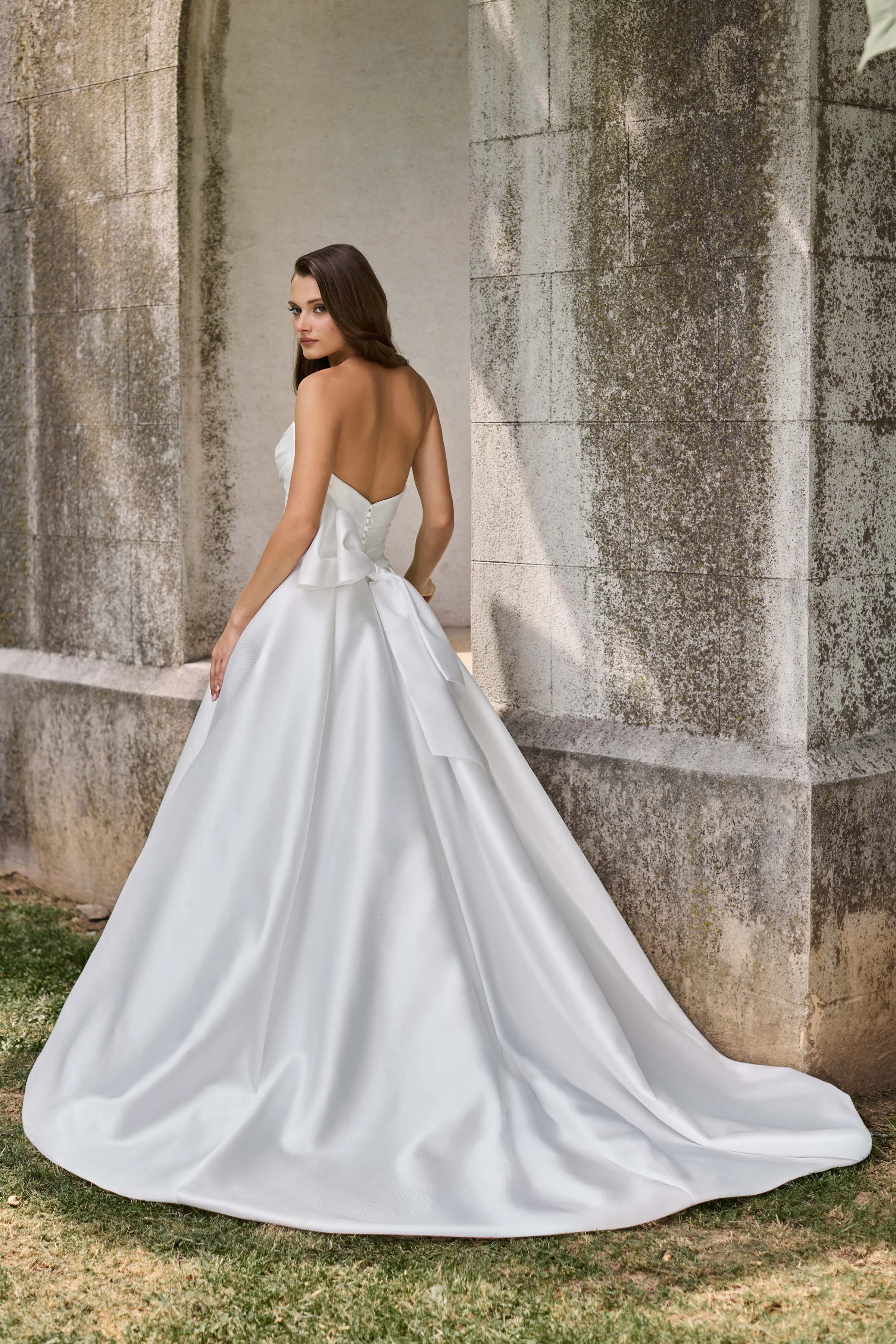 Back view of a strapless Mikado wedding dress with buttons on the back bodice and a back bow, with an A-line skirt.
