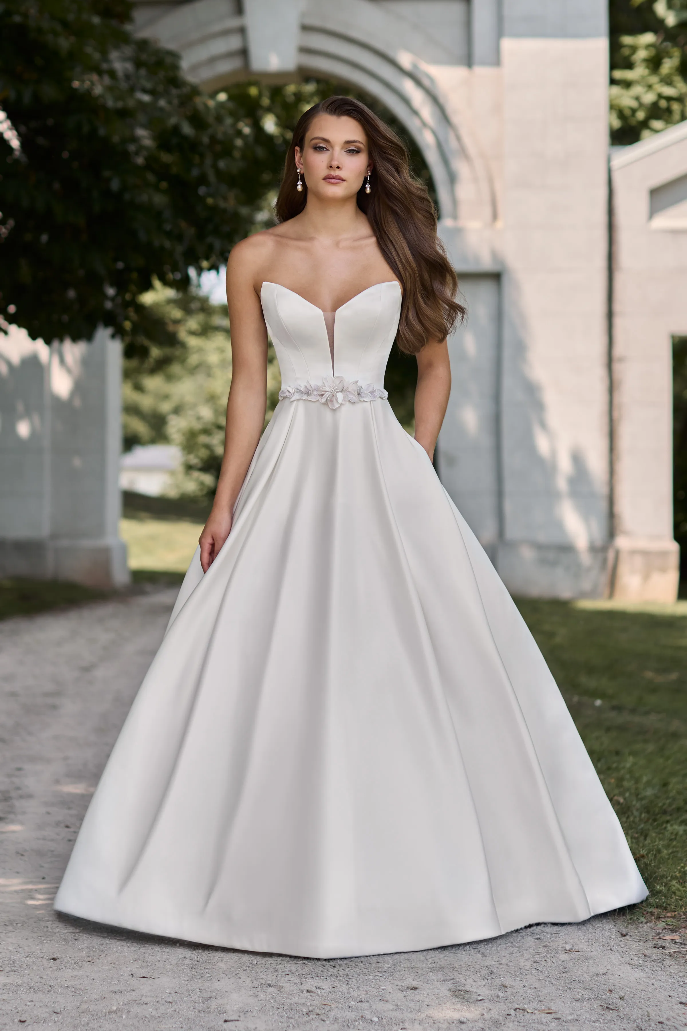 Satin gown with strapless plunging neckline and floral belt, with a pleated Satin skirt with pockets.