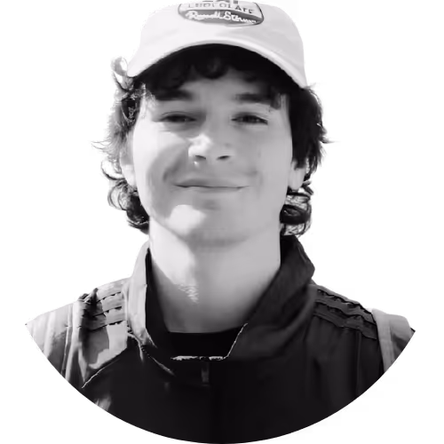 Young man smiling, wearing a light-colored cap and a zippered jacket.