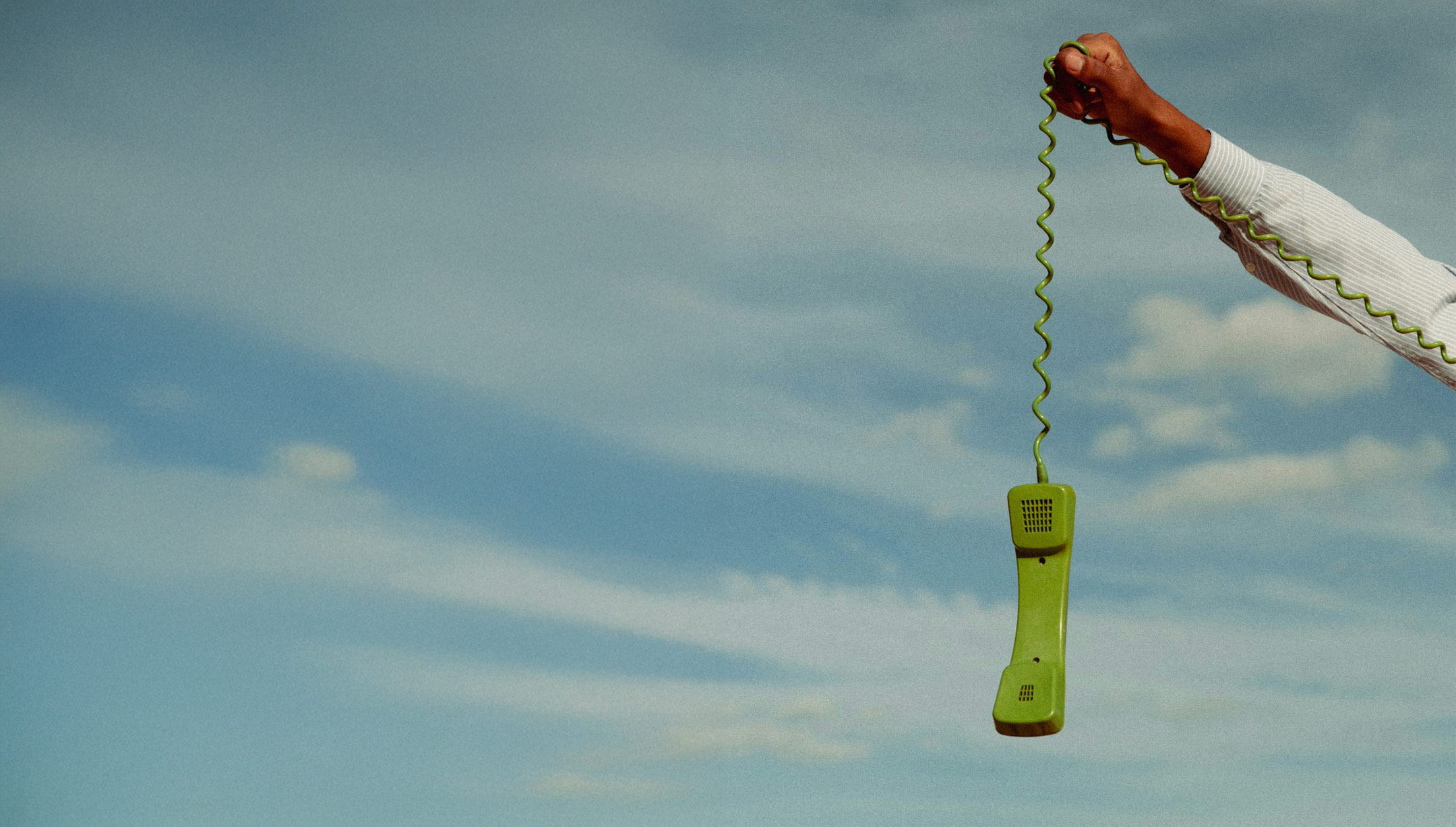 Combiné téléphonique vert tenu en l’air sur fond de ciel bleu