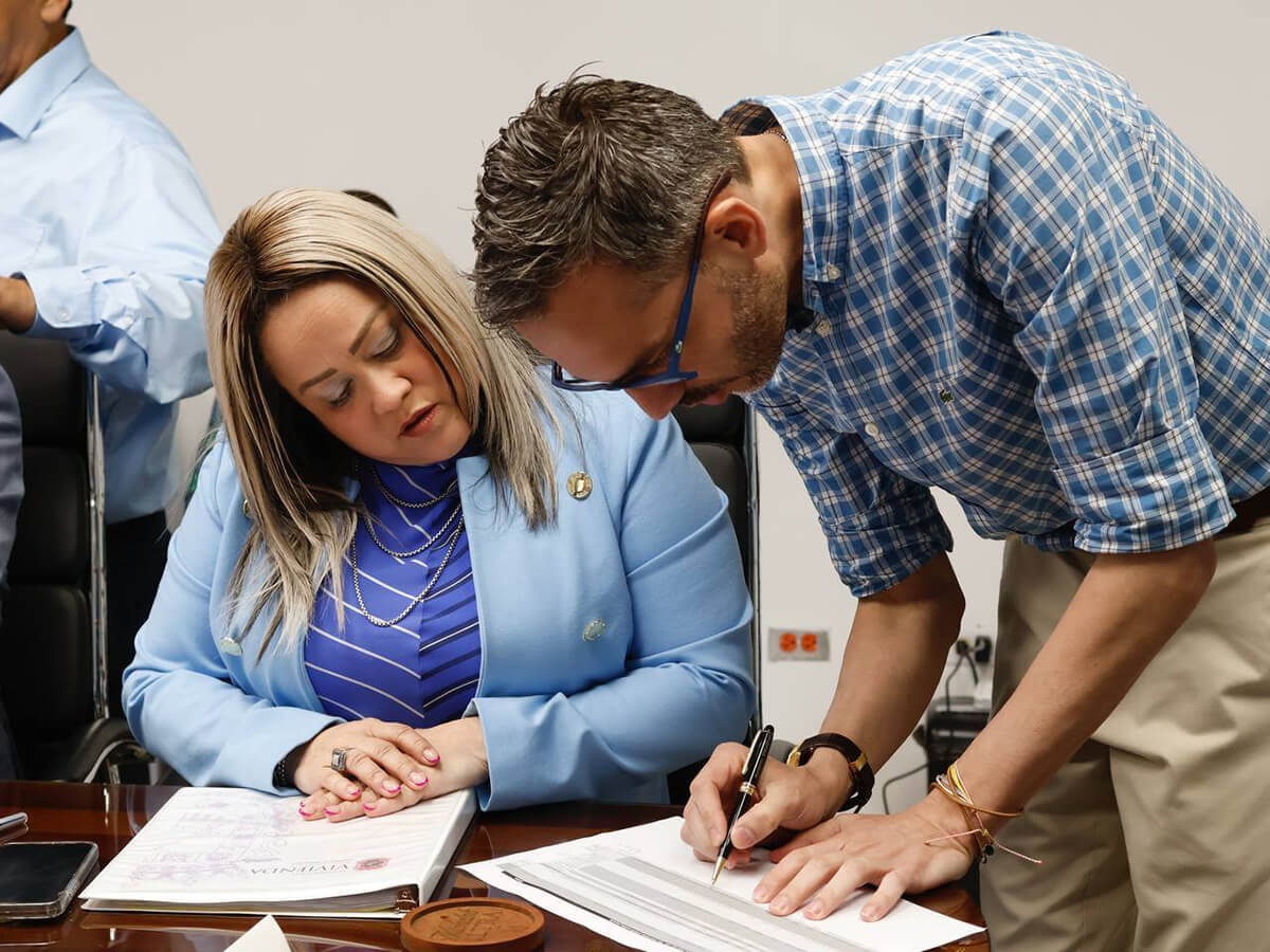 Ciary Pérez Peña mirando documento que es firmado por otra persona.