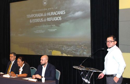 Una hablando en el microfono frente a la pantalla de la presentación y 3 personas sentadas.