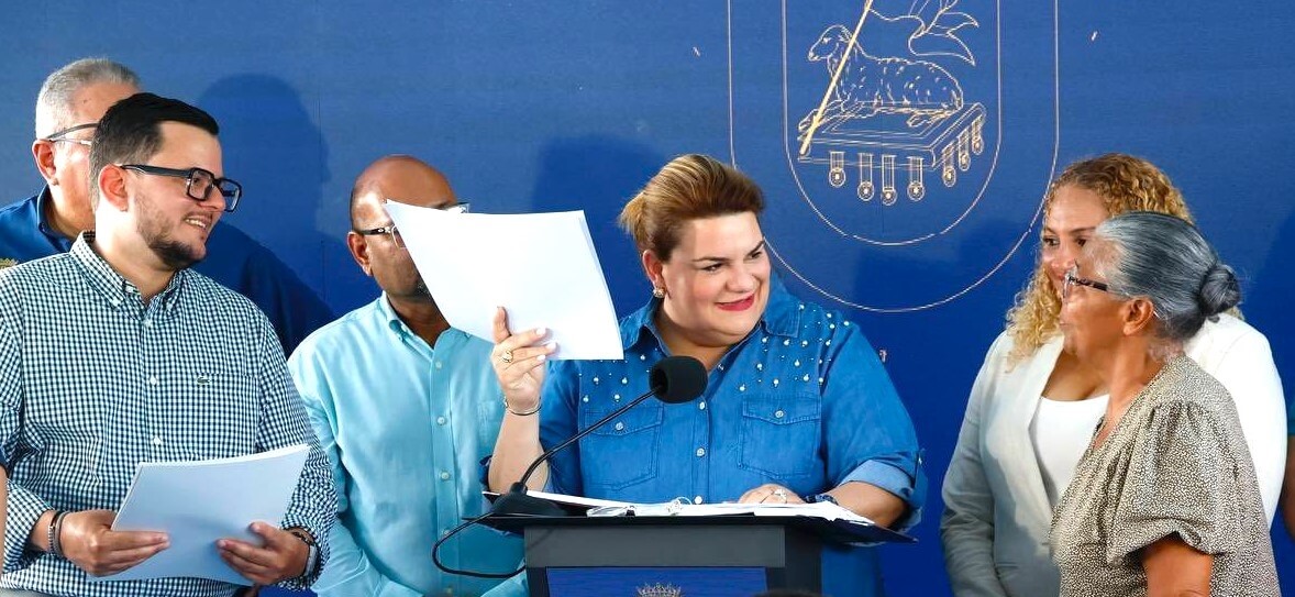 Governor Jenniffer González Colón on stage holding papers with three people.