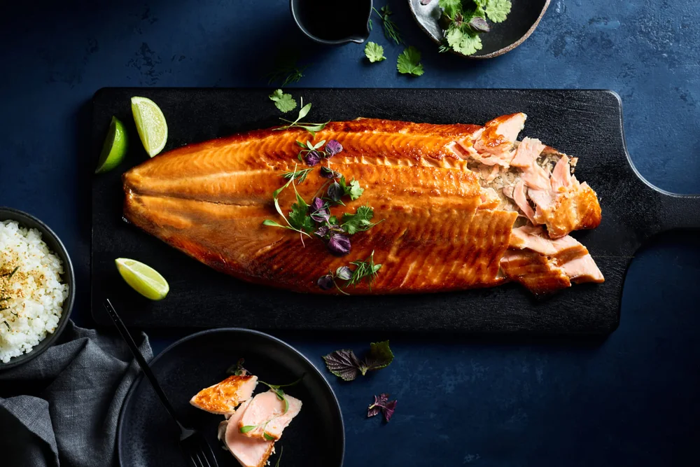 Huon salmon served with lime and herbs on a dark serving board