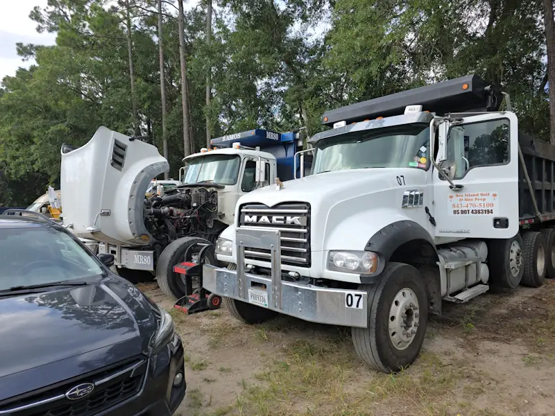 Truck repair on Mack dump trucks with one hood raised, exposing the engine for diagnostics, maintenance, and heavy-duty repair service.