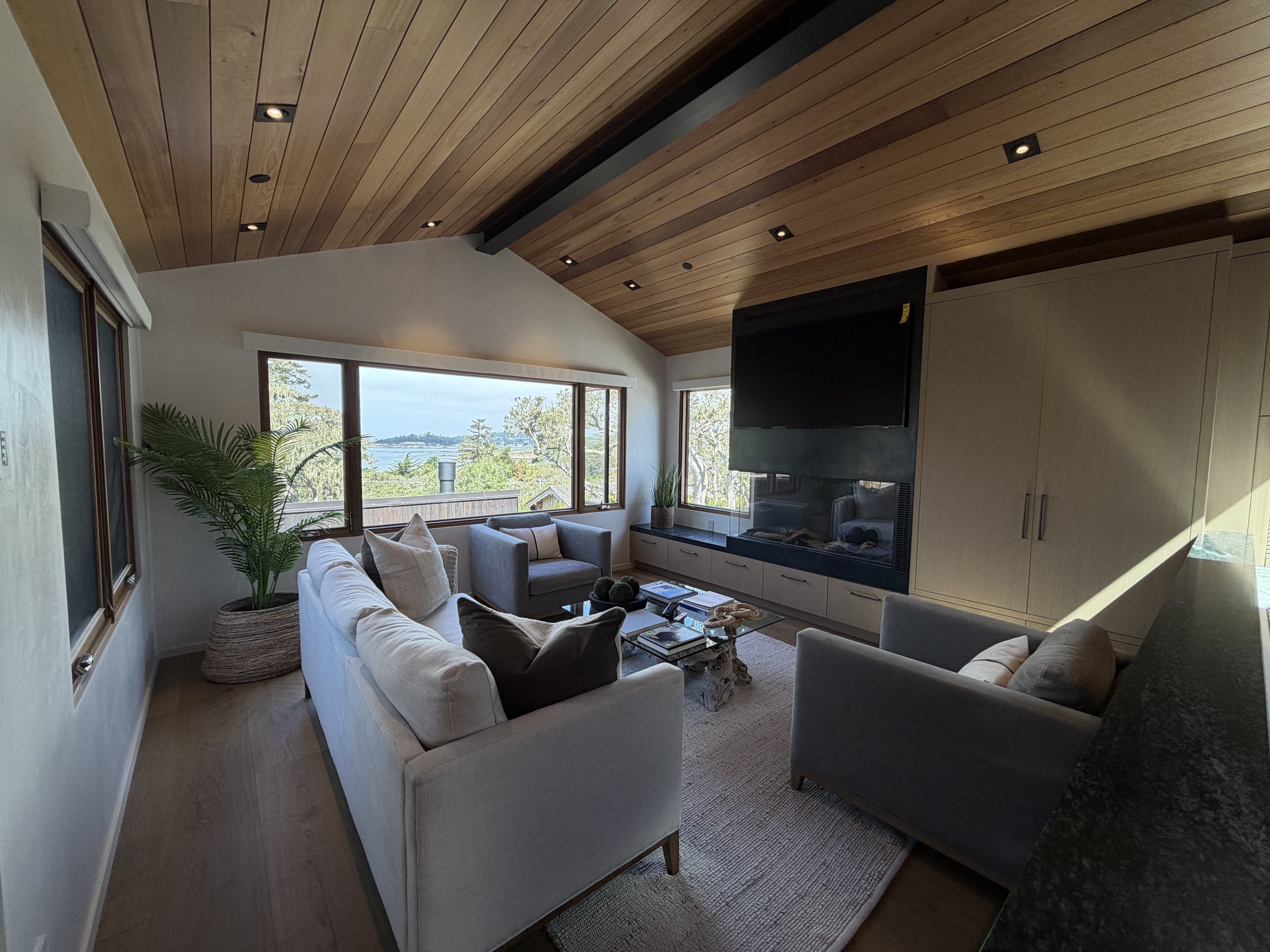 Brisa living room with ocean view windows, fireplace, and cathedral wood ceiling