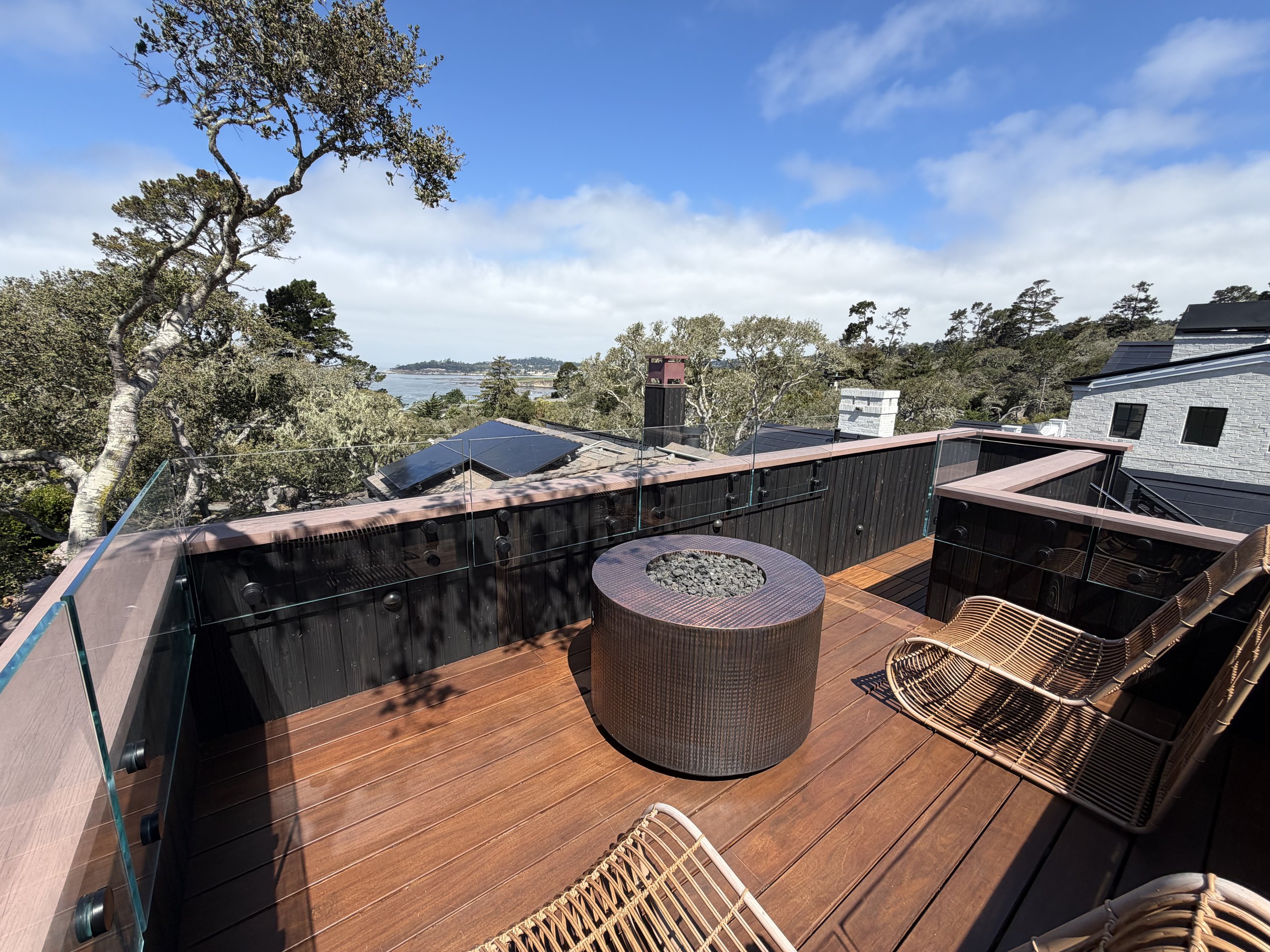 Roof deck at Brisa with fire pit, glass railings, and views toward Carmel Bay