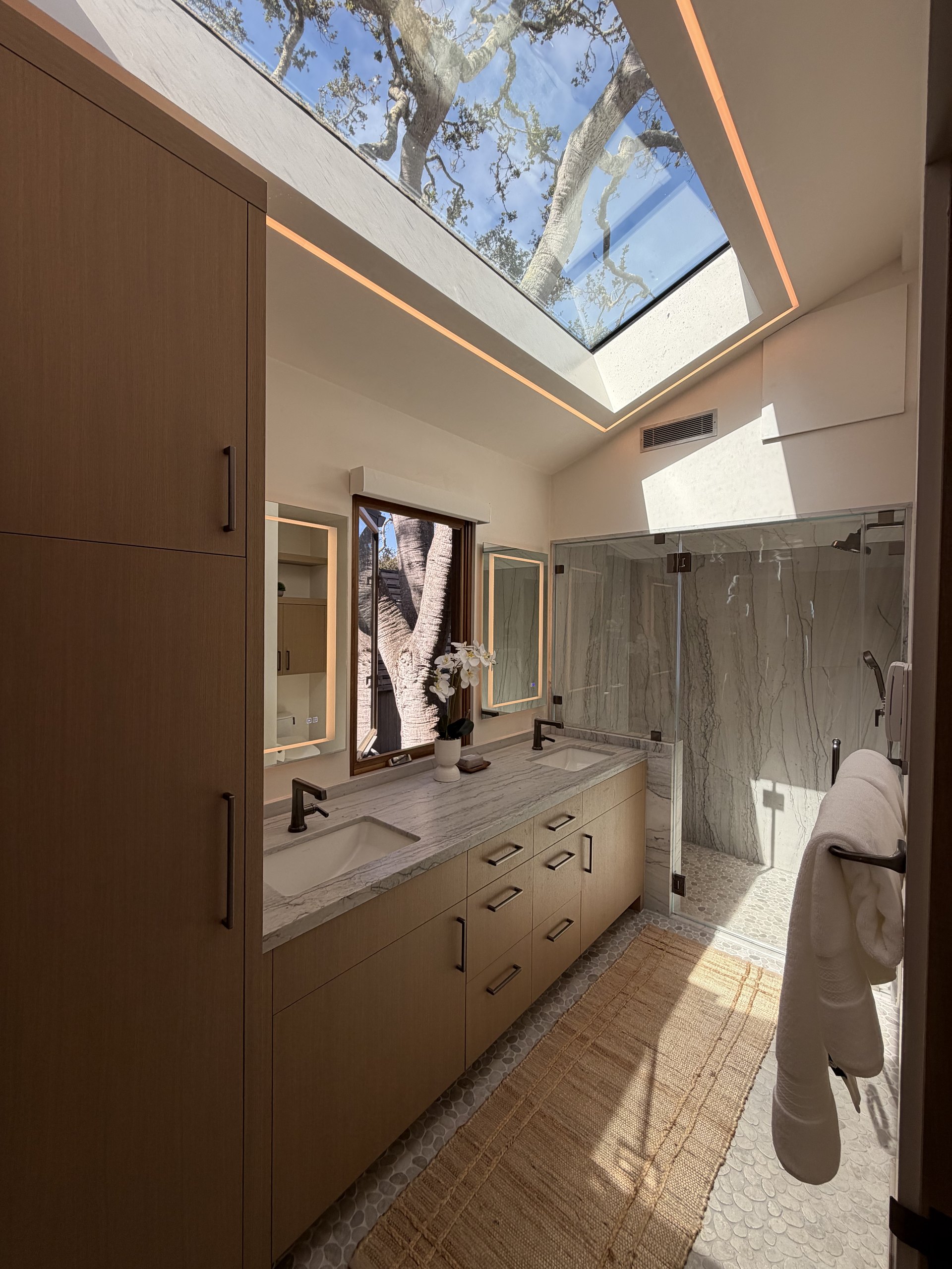 Primary bathroom at Brisa with a large skylight framing the oak canopy above the double vanity and stone shower