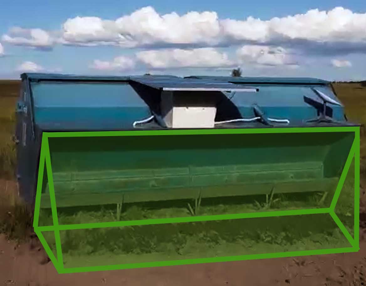 Blue metal container with a white box attached under the lid, sitting on dirt and grass under a partly cloudy sky.
