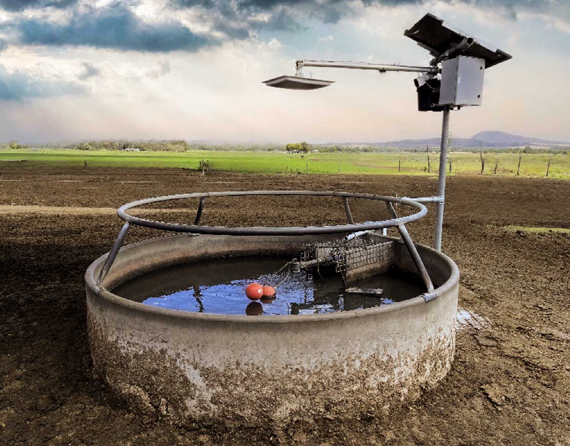 Outdoor livestock water trough with a metal frame and attached solar panel set in a muddy field under a cloudy sky.