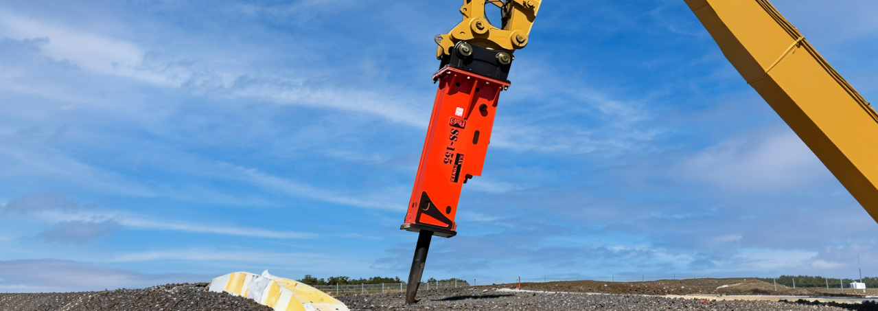 Modern excavator equipped with a red and white SWT hydraulic breaker operating on a dynamic construction site.