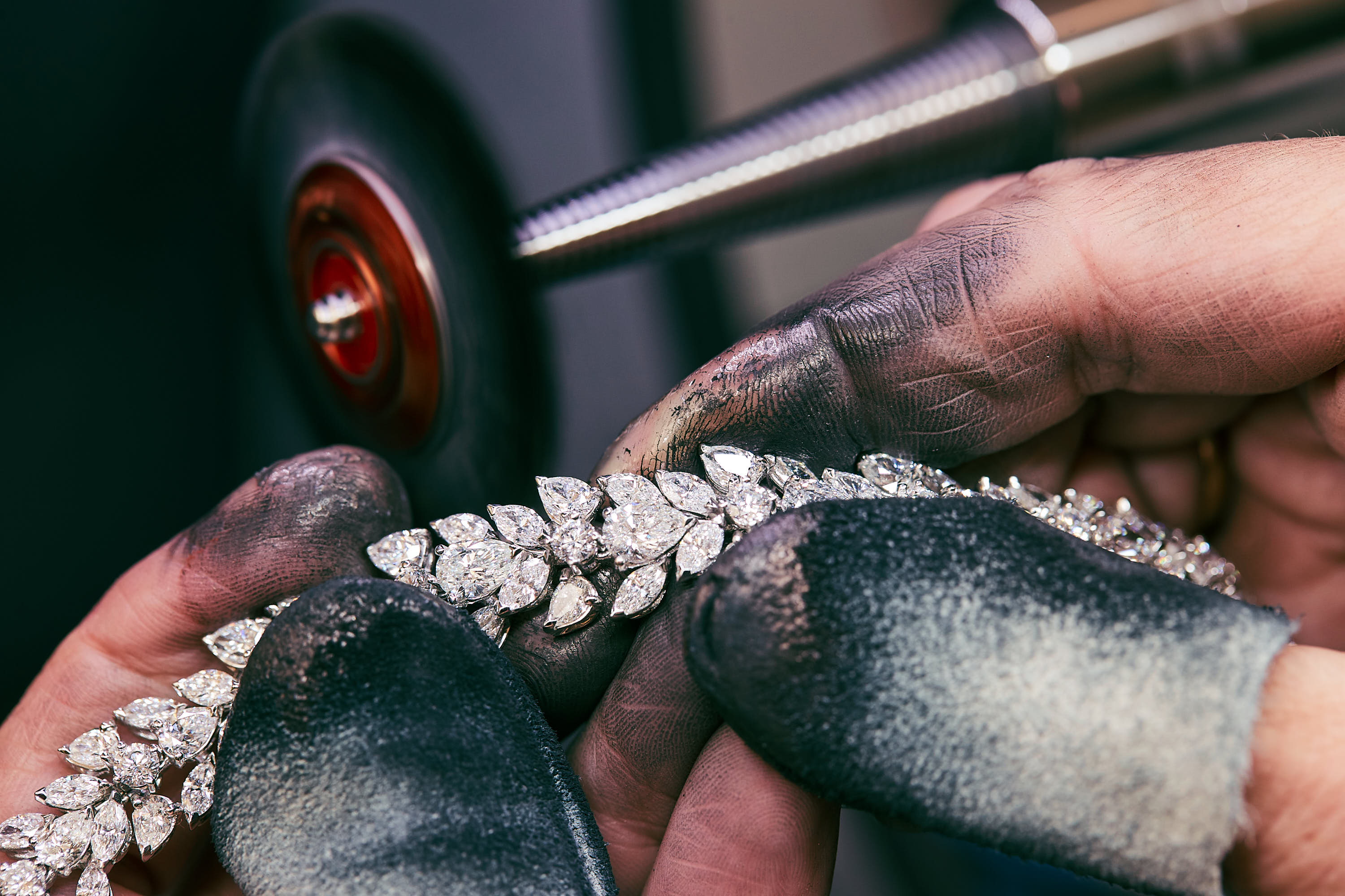 Nahaufnahme von stark verschmutzten Händen, die einen glitzernden Diamantarmband bearbeiten.