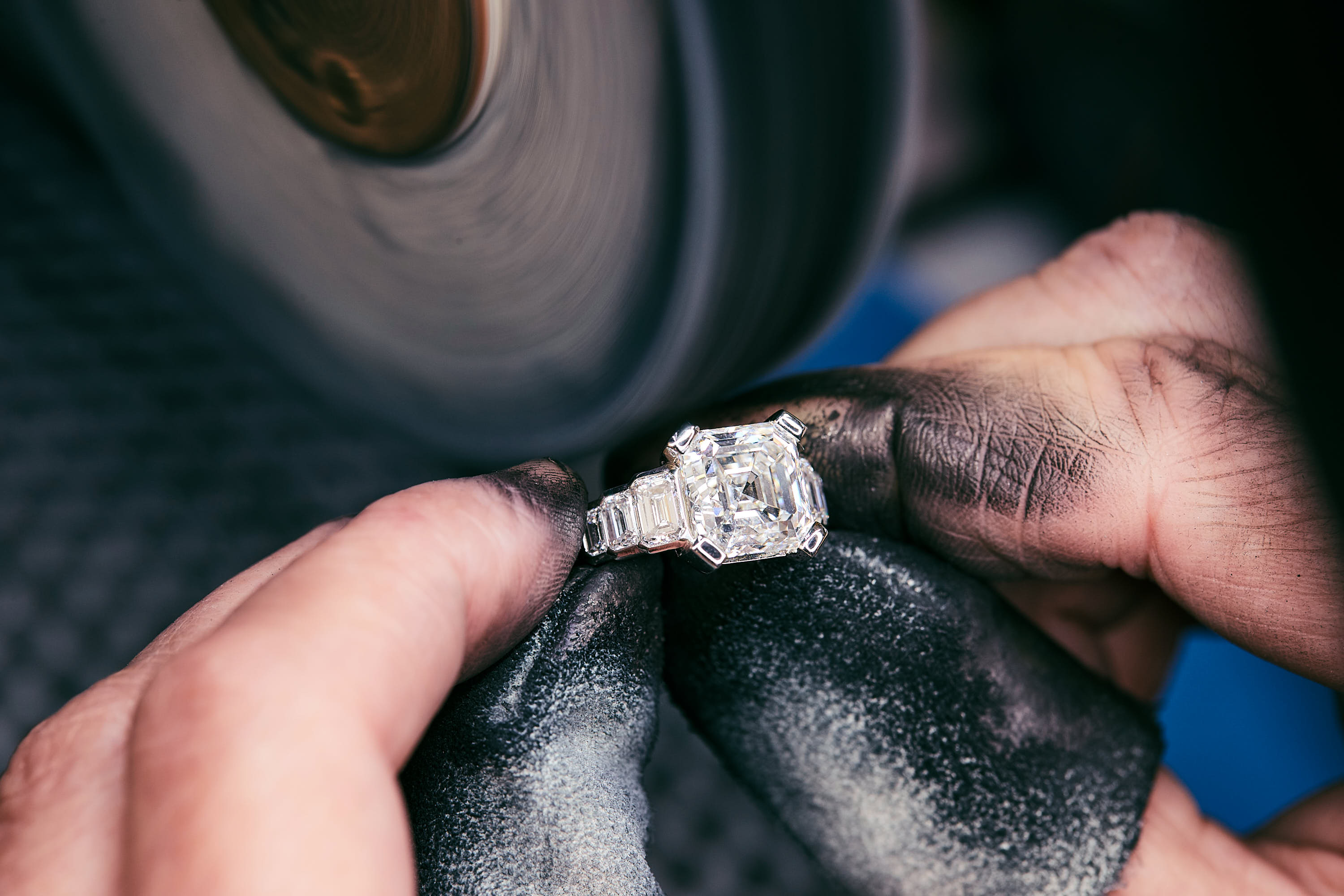 Hand poliert mit einem Poliertuch einen Ring mit einem großen quadratischen Diamanten und mehreren kleineren Diamanten.