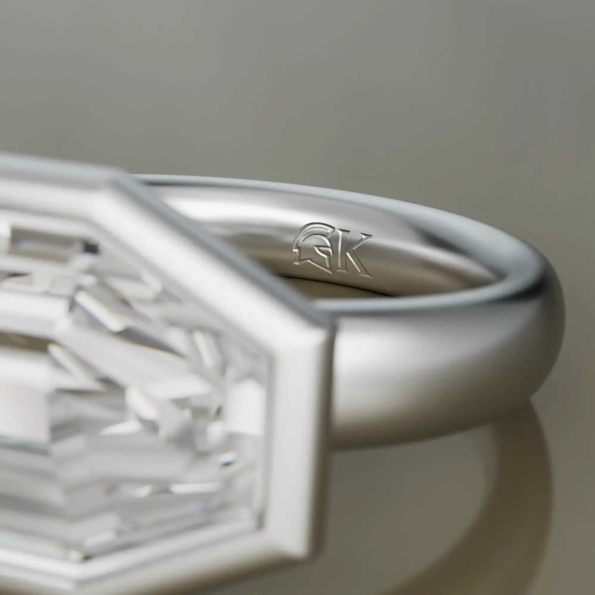 Nahaufnahme eines silbernen Rings mit einem eingravierten Helm-Logo und dem Buchstaben K im Inneren.