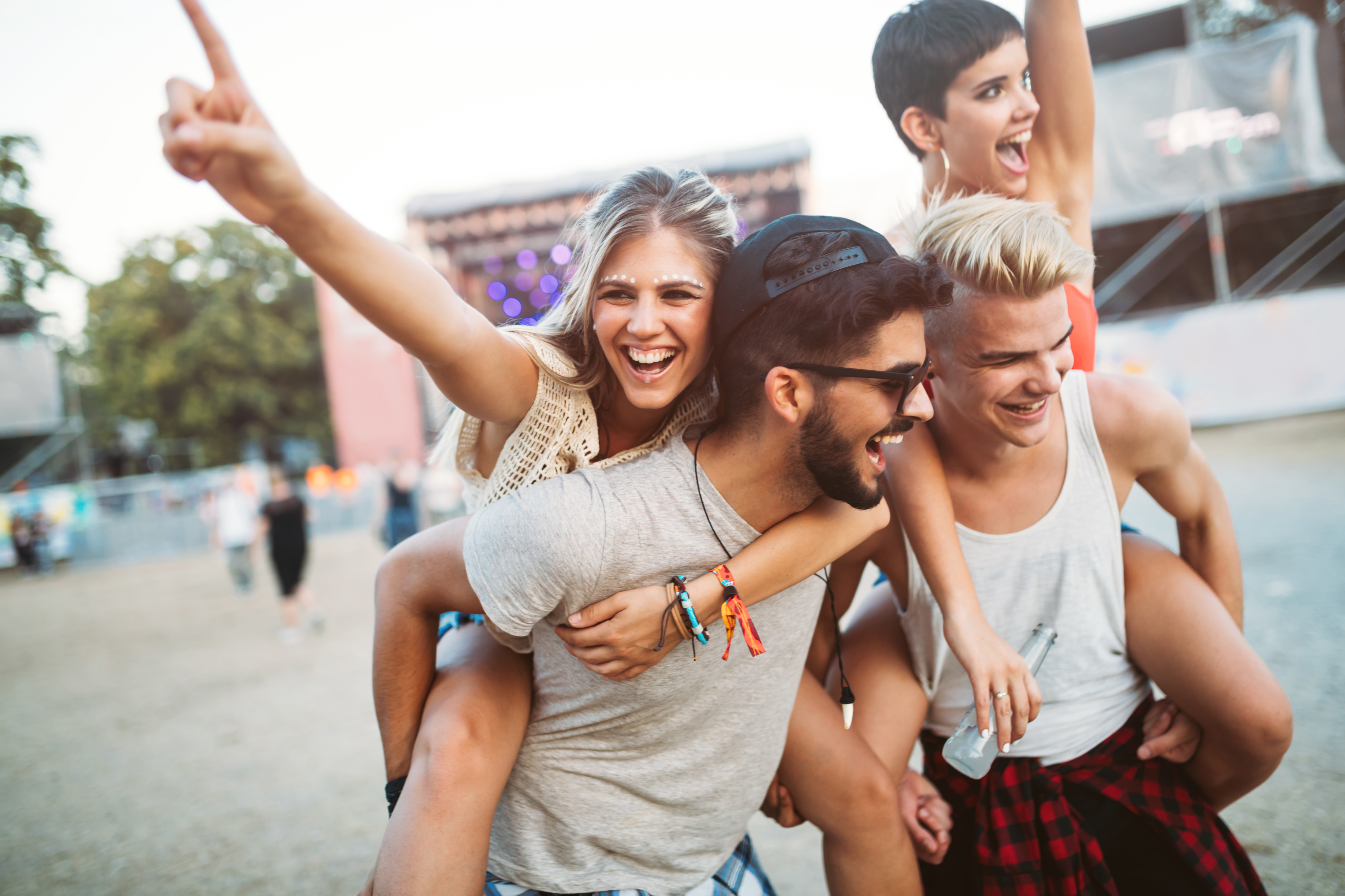 Vier junge Erwachsene lachen und genießen ein Festival mit zwei Frauen auf den Rücken der Männer.