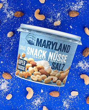 Becher mit Maryland Snack Nüsse, geröstet und gesalzen, umgeben von verschiedenen Nüssen auf blauem Hintergrund.