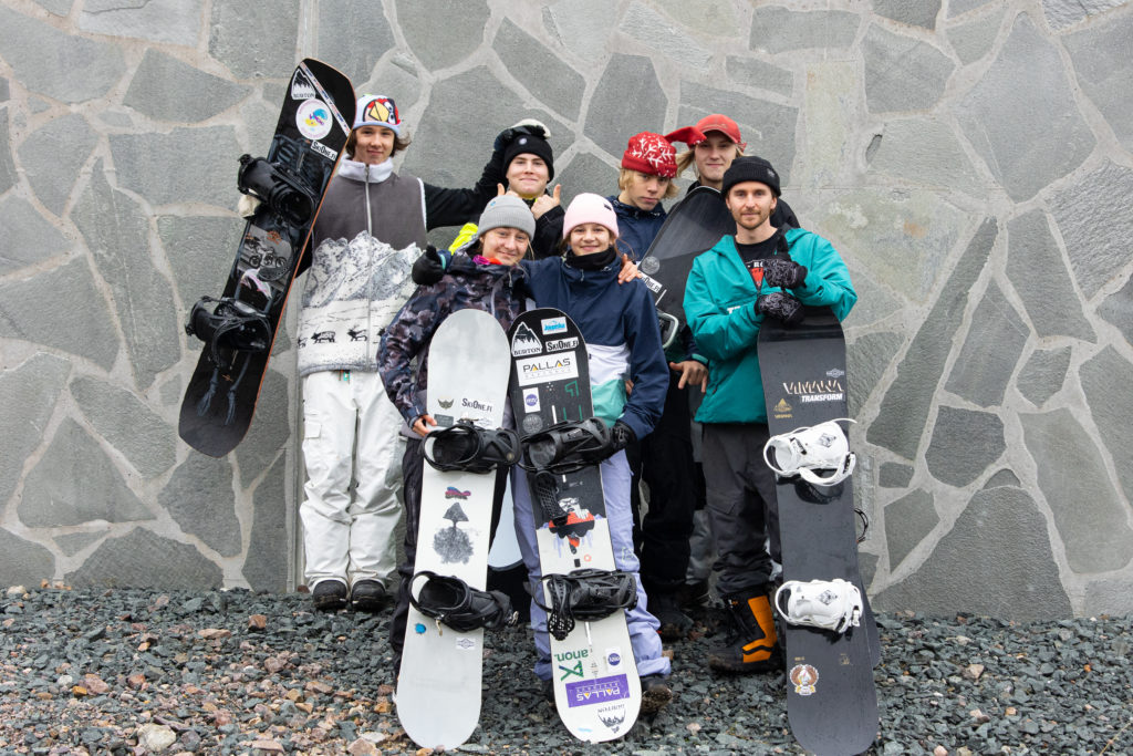 Teenagers with the snowboards standing near a wall, looking at the camera and smiling