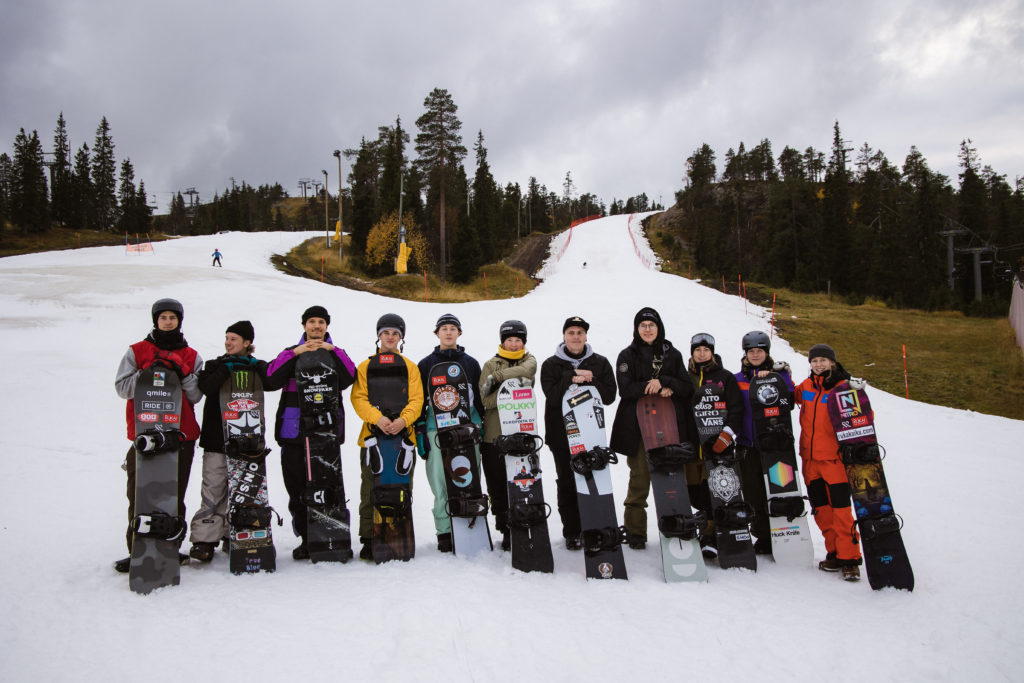 Snowboarders standing near slopes with the snowboards, looking at the camera and smiling